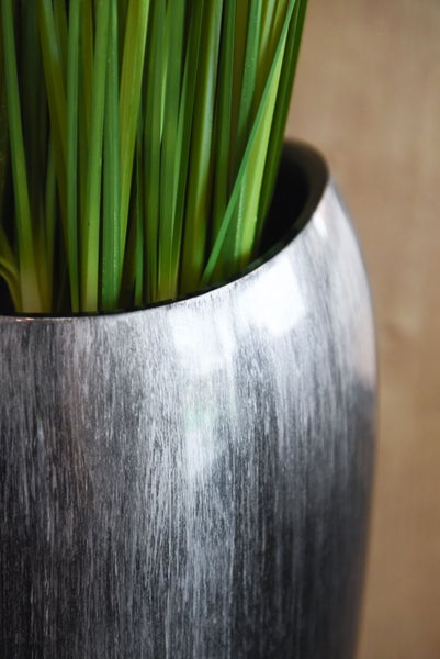 Künstliches Gras in einem bauchigen Dekotopf mit strukturierter grau-weißer Oberfläche.