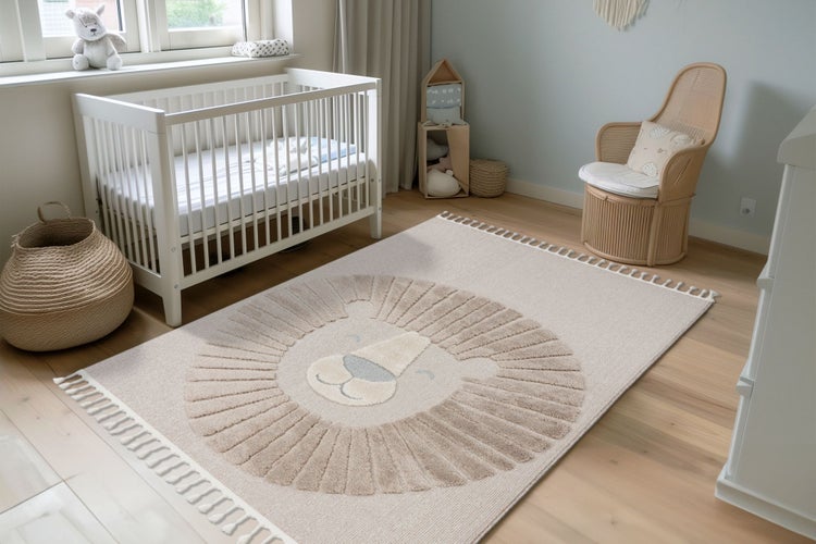 Kinderspielteppich mit Löwenmotiv und Fransen in einem gemütlich eingerichteten Babyzimmer mit Gitterbett und Rattan Sessel.