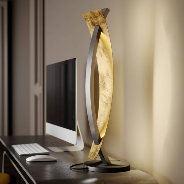 Moderne Tischleuchte mit zwei geschwungenen Elementen in Metall und Gold-Optik auf einem dunklen Holzschreibtisch, warmweiße Beleuchtung.