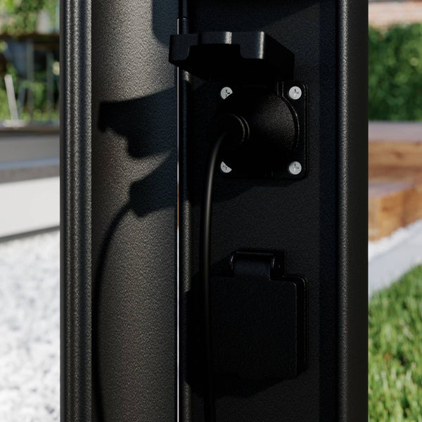 Schwarze Außensteckdosensäule mit zwei Steckdosen, eine mit eingestecktem Kabel und eine mit geschlossenem Klappdeckel im Garten.