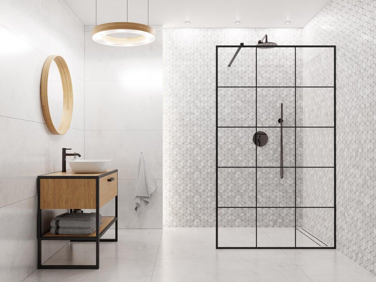 Helles Badezimmer mit begehbarer Dusche, Glaswand mit schwarzem Rahmen im Industriedesign, Waschtischunterschrank aus Holz, runder Holzspiegel und geometrische Wandfliesen.