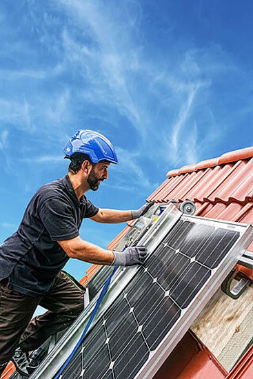 Mann mit Schutzhelm montiert Solaranlage auf Dach