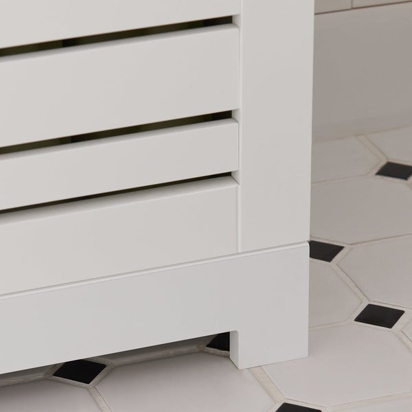 Detailansicht eines weißen Badezimmerschranks mit Lamellentüren und Füßen auf einem gefliesten Badezimmerboden