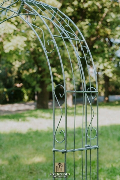 Detailansicht eines Rosenbogens aus Metall im Garten.