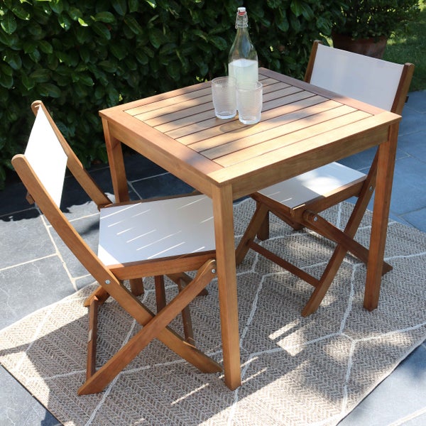 Balkonset aus Holz mit einem quadratischen Tisch und zwei Klappstühlen mit weißer Bespannung auf einer Terrasse.