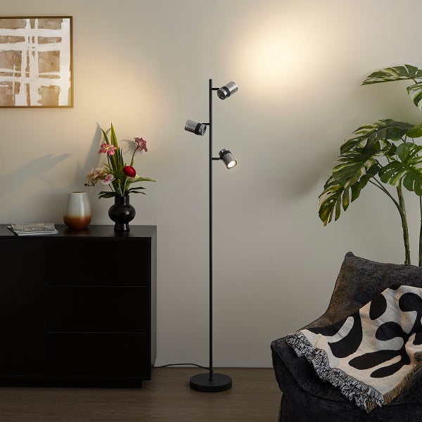 Moderne schwarze Stehleuchte mit drei verstellbaren Spots in einer Wohnzimmerumgebung neben einer Kommode und einer Pflanze.