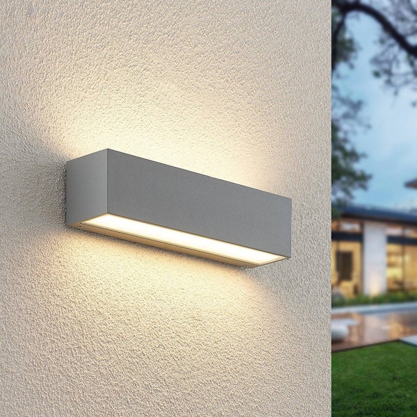 Moderne, rechteckige Außenwandleuchte in Grau an einer strukturierten Hauswand. Strahlt warmweißes Licht nach oben und unten ab.