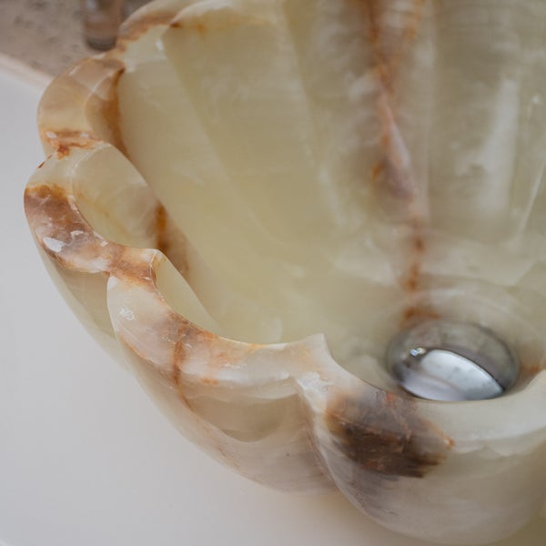 Nahaufnahme eines muschelförmigen Waschbeckens aus Onyx mit natürlicher Maserung und verchromtem Ablauf.