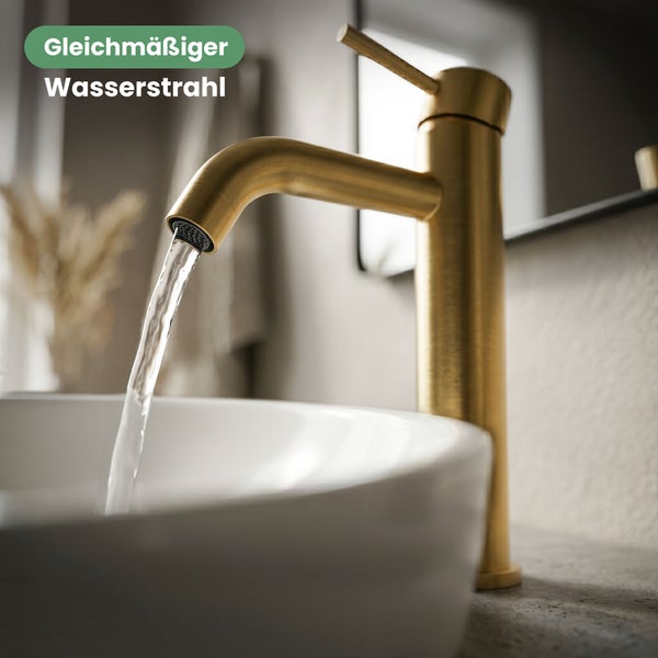 Goldfarbene Waschtischarmatur mit gleichmäßigem Wasserstrahl in einem weißen Waschbecken in einem modernen Badezimmer.