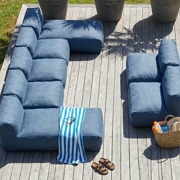 Modernes modulares Outdoor-Lounge-Sofa-Set aus Stoff auf einer Holzterrasse mit sommerlichen Accessoires.