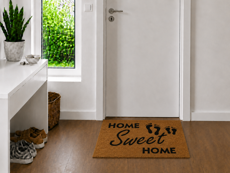 Fußmatte aus Kokos mit Schriftzug Home Sweet Home vor einer weißen Tür in einem hellen Eingangsbereich mit Holzfußboden.