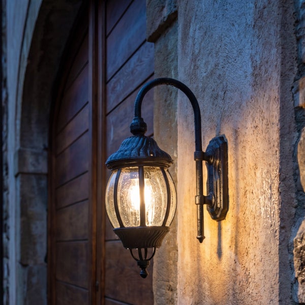 Rustikale Außenwandleuchte aus schwarzem Metall mit rundem Glas und eingeschaltetem Licht, montiert an einer Steinwand.