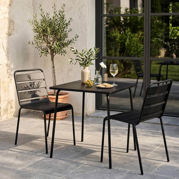 Modernes Gartenmöbel-Set aus schwarzem Metall mit quadratischem Bistrotisch und zwei Lattenstühlen auf einer Steinterrasse.