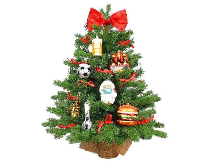 Geschmückter künstlicher Weihnachtsbaum in einem Jutesack mit verschiedenen Anhängern und einer großen Schleife an der Spitze.