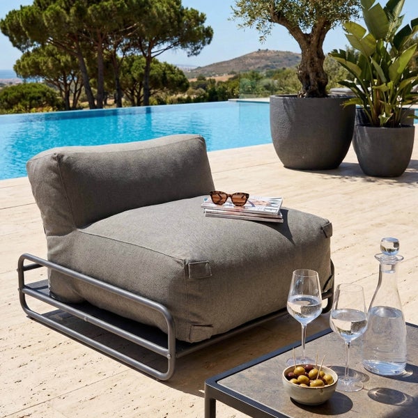 Moderner Garten-Loungesessel mit grauem Polster auf einem Metallgestell neben einem Pool auf einer sonnigen Terrasse.
