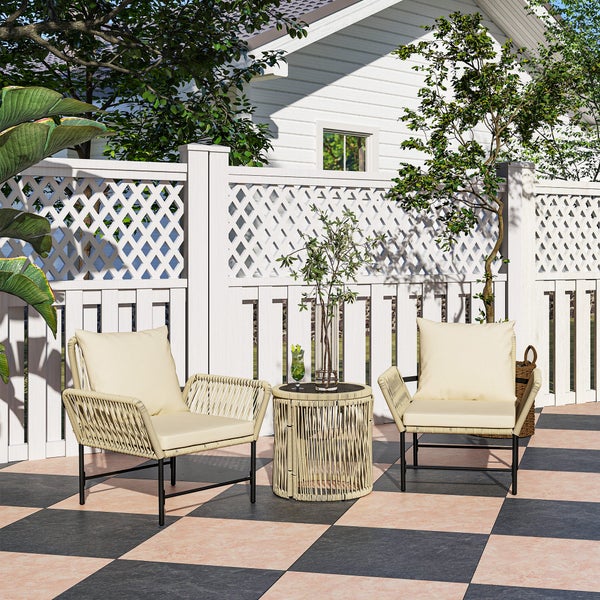 Gartenszene mit zwei Korbsesseln, Beistelltisch und Dekoration vor einem weißen Gartenzaun.