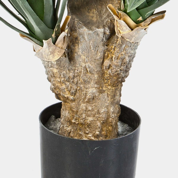 Detailaufnahme einer künstlichen Yucca-Palme mit strukturiertem Stamm und grünen Blättern in einem schwarzen Topf.