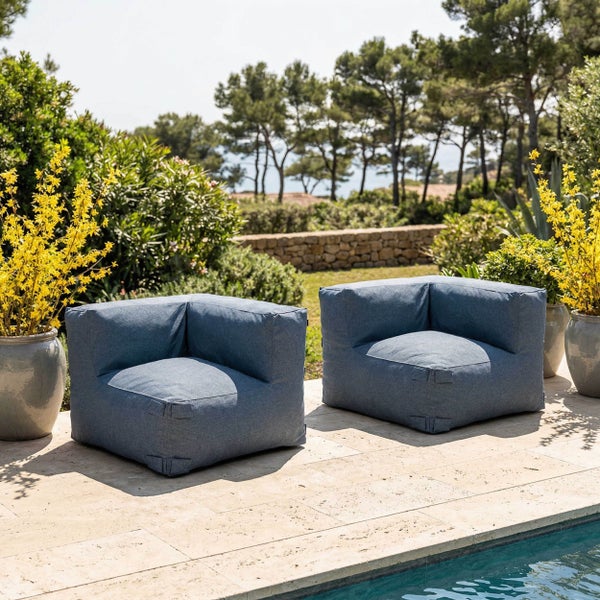 Zwei blaue Outdoor-Lounge-Sessel auf einer Steinterrasse am Pool, umgeben von grünen Sträuchern und gelben Blumen.