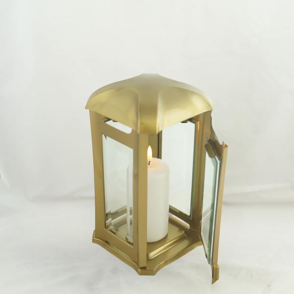 Goldfarbene Laterne aus Metall mit Glasfenstern und brennender Stumpenkerze