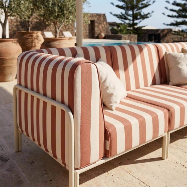 Modernes Garten-Sofa mit weißem Metallgestell und gestreiften Polstern in Terrakotta und Weiß auf einer hellen Terrasse am Pool.