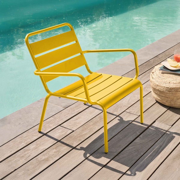 Gelber Gartenstuhl aus Metall mit Armlehnen und Lamellenstruktur auf einer hellen Holzterrasse an einem Pool.