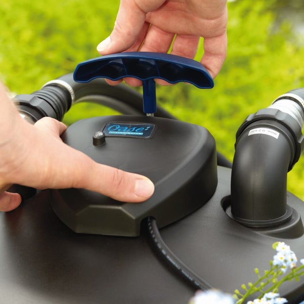 Hände bedienen den blauen Reinigungsgriff eines schwarzen Oase Teichdruckfilters mit Schlauchanschlüssen.