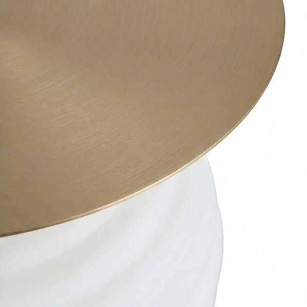 Detailansicht einer runden Metallplatte in gebürsteter Goldoptik auf einem weiß strukturierten Sockel.