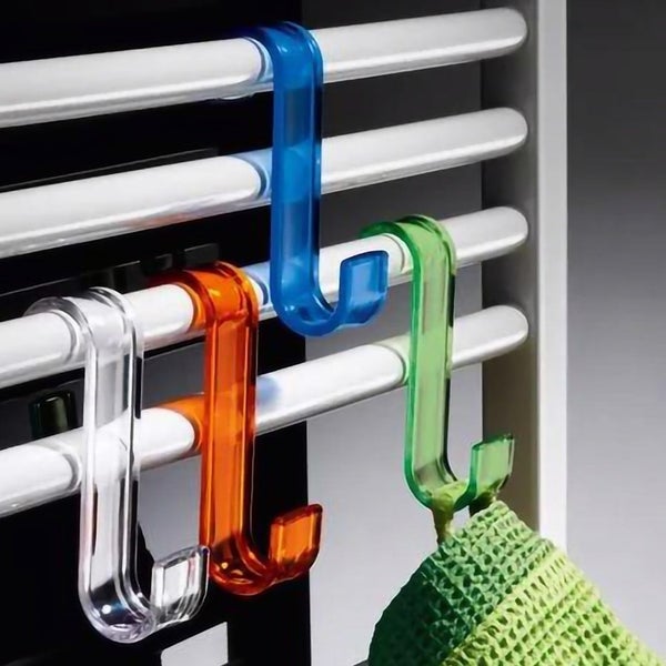 Vier farbige transparente Kunststoffhaken an einem weißen Handtuchheizkörper, an einem grünen Haken hängt ein Waschlappen.