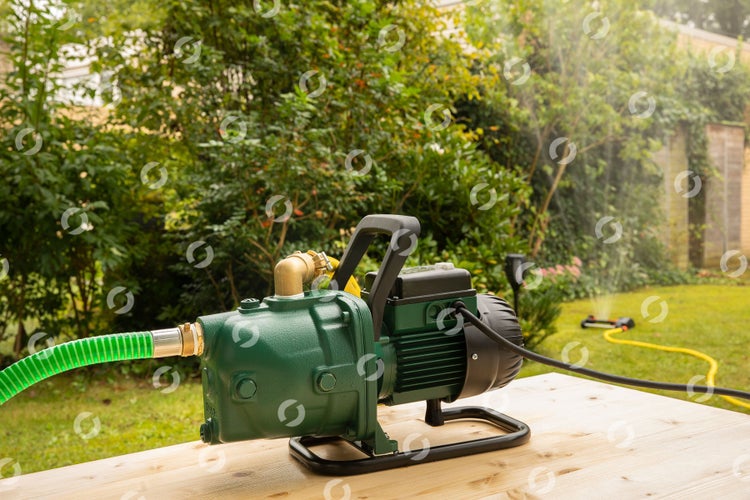 Gartenwasserpumpe auf einem Holztisch mit einem Rasensprenger im Hintergrund