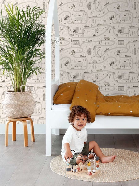 Kinderspielzimmer mit Kindertapete mit Straßenmotiv, weißem Holzbett, Topfpflanze im Korb und einem Kind, das auf dem Boden spielt.