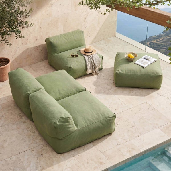Modernes Outdoor-Lounge-Set auf einer hellen Steinterrasse, bestehend aus einem Zweisitzer-Sessel, einem Einzelsessel und einem quadratischen Hocker aus Textil.