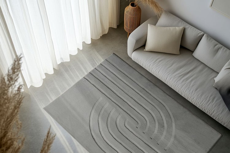 Wohnzimmer mit modernem Teppich mit abstraktem Linienmuster vor einem Sofa mit Kissen und Vorhängen in einem hellen, wohnlichen Ambiente.