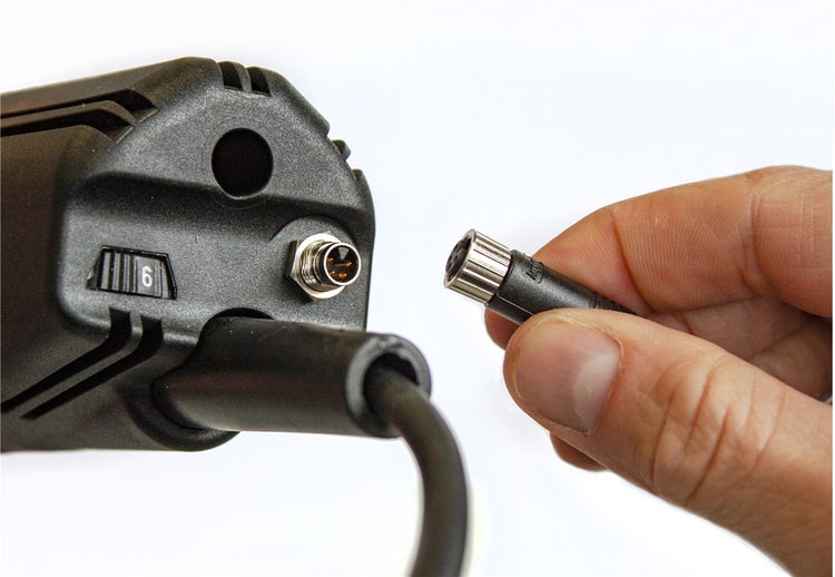 Hand beim Einstecken eines runden elektrischen Steckers in die Buchse eines Elektrowerkzeugs