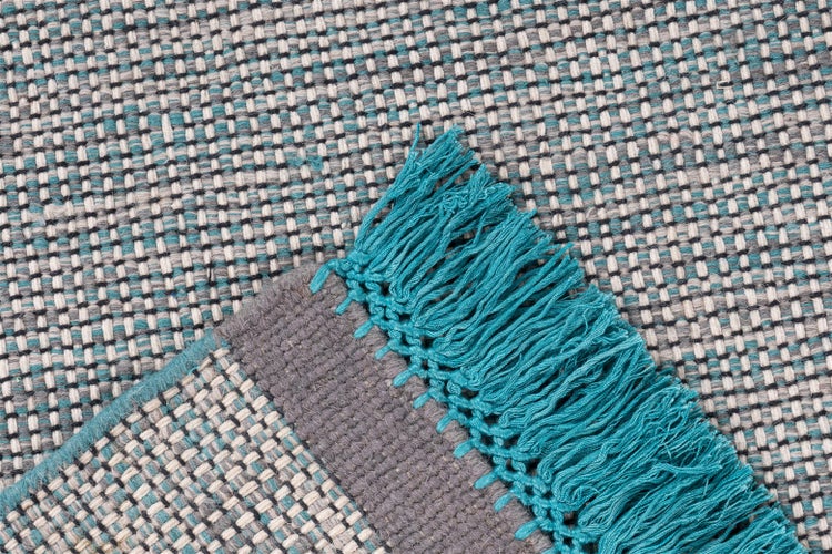 Flachgewebter Teppich in Türkis und Grau mit Fransen und Karomuster.