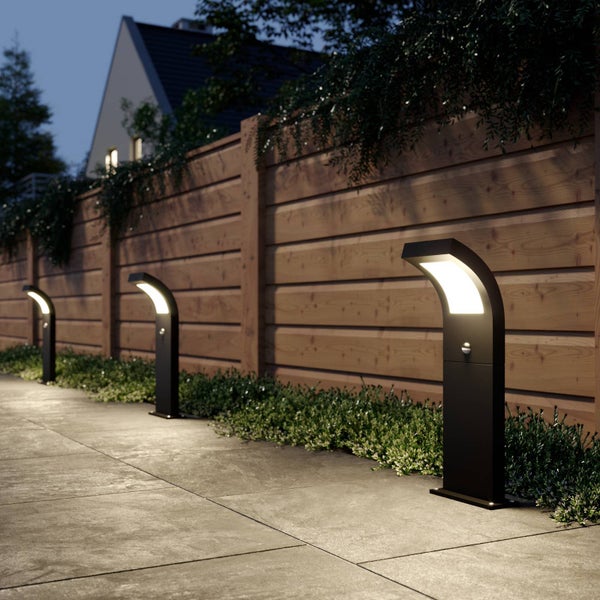 Moderne schwarze Wegleuchten mit Bewegungsmelder beleuchten einen Steinpfad neben einem Holzzaun bei Nacht.