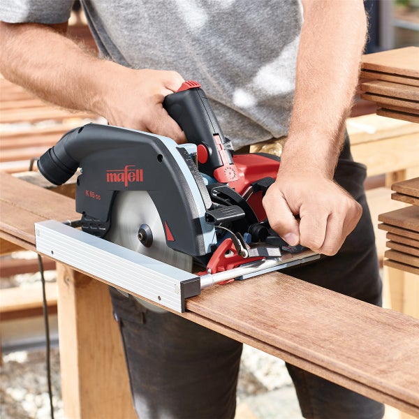 Handwerker beim Zuschneiden eines Holzbretts mit einer Mafell K 65 cc Handkreissäge auf einer Werkbank.