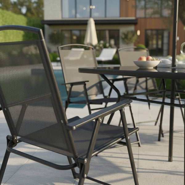 Moderne Sitzgruppe auf einer Terrasse mit Klappstühlen aus Metall und Netzgewebe an einem Tisch, Pool und Haus im Hintergrund.