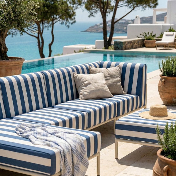 Gestreiftes Outdoor-Lounge-Set mit blau-weißem Muster auf einer hellen Terrasse an einem Pool mit Aussicht auf das Meer.