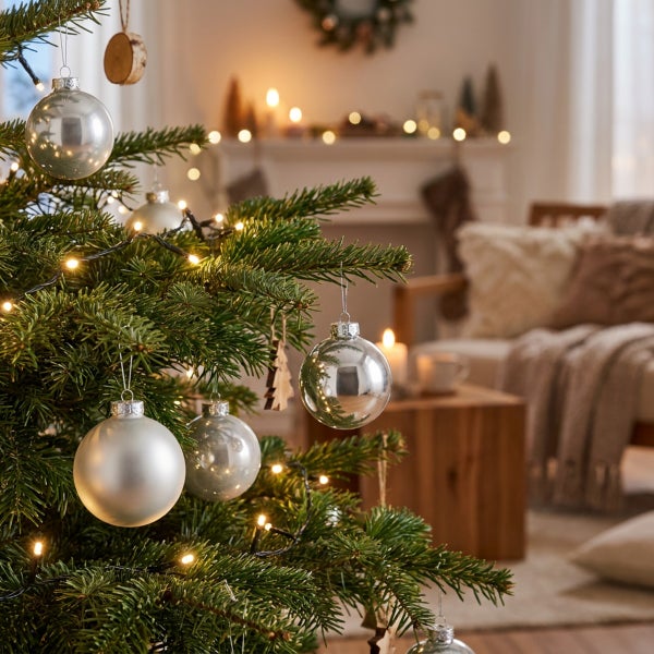 Geschmückter Weihnachtsbaum mit glänzenden und matten Kugeln und Lichterkette im festlich dekorierten Wohnzimmer.