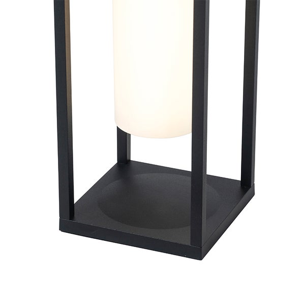 Detailaufnahme einer modernen Lampe mit schwarzem Metallgestell und weißem zylindrischem Diffusor auf quadratischem Standfuß.