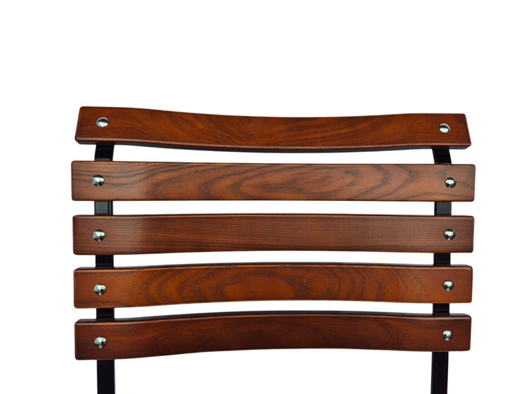 Rückenlehne aus gebogenen Holzlatten mit Maserung und sichtbaren Schrauben an einem schwarzen Metallrahmen.
