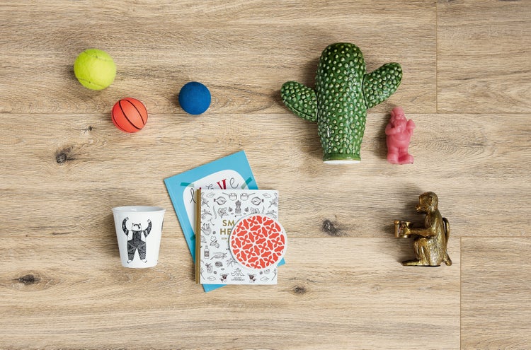 Draufsicht auf einen Bodenbelag aus Laminat in Holzoptik mit verschiedenen Dekoartikeln wie einer Kaktusfigur, einem Becher und Spielzeug.