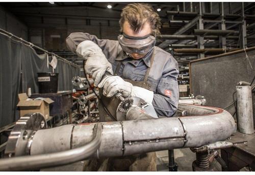 Ein Arbeiter mit Schutzbrille bearbeitet ein Metallrohr mit einer Schleifmaschine.