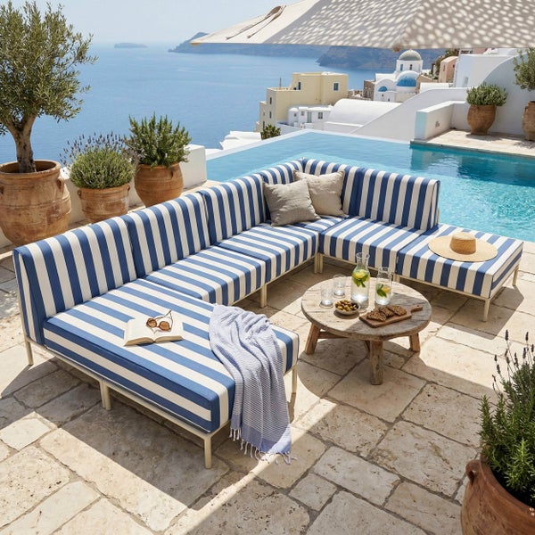 Helle, L-förmige Outdoor-Lounge-Gruppe mit blau-weiß gestreiften Polstern auf einer Steinterrasse neben einem Pool mit Meerblick und Holztisch.
