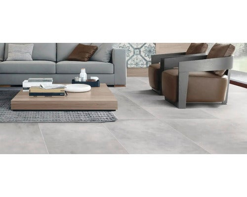 Wohnzimmer mit großen grauen Bodenfliesen in Betonoptik, kombiniert mit moderner Sitzgruppe aus Sofa und zwei Sesseln auf einem Teppich.