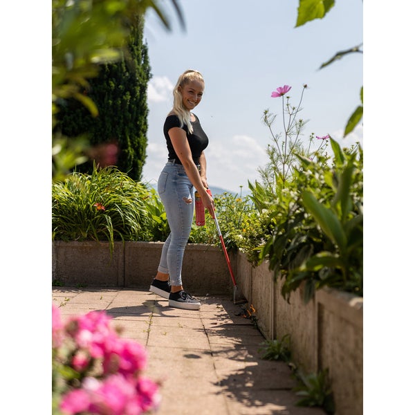 Frau verwendet einen Fugenkratzer, um Unkraut zwischen Pflastersteinen zu entfernen.