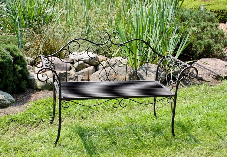 Verschnörkelte Gartenbank aus Metall mit dekorativen Ornamenten und Lattensitz auf einer Rasenfläche.