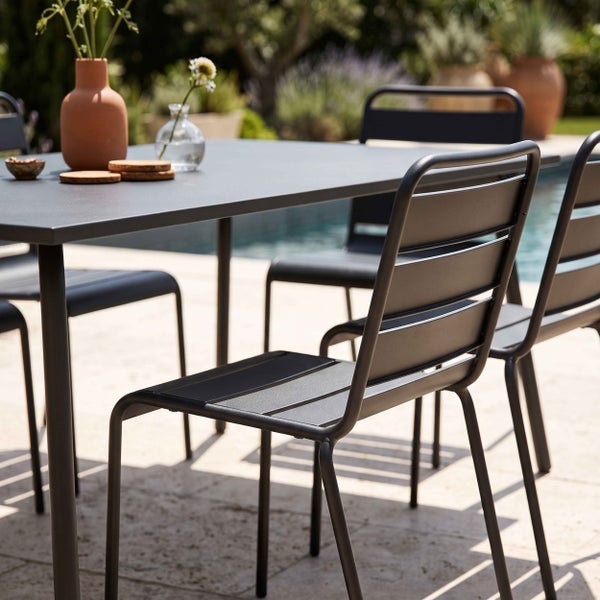 Modernes Gartenmöbel-Set aus Metall mit Tisch und Stühlen in Lamellenoptik auf einer hellen Steinterrasse am Pool.