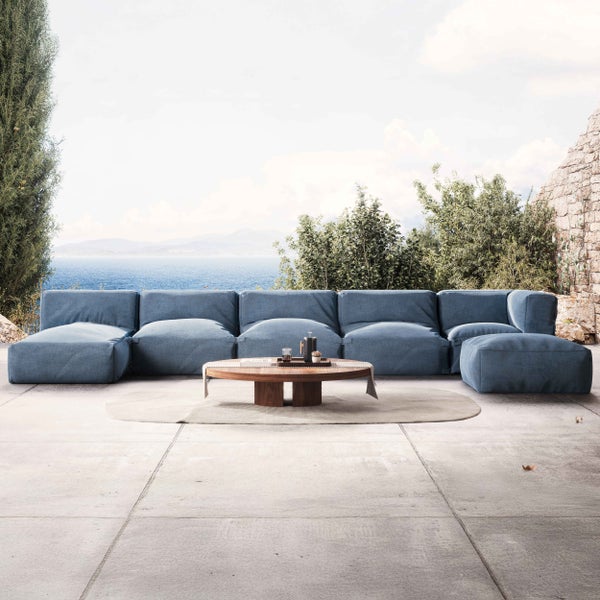 Moderne blaue modulare Gartenlounge auf einer hellen Steinterrasse mit rundem Couchtisch aus Holz vor Meerblick.