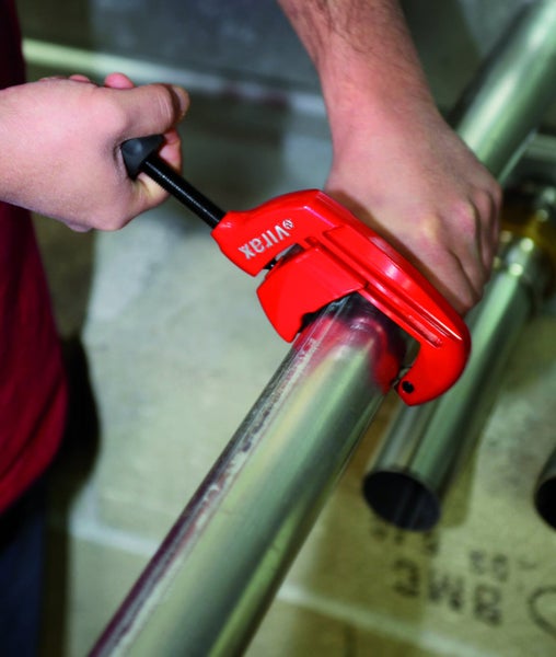 Hände benutzen einen Virax Rohrabschneider zum Schneiden eines Metallrohrs.